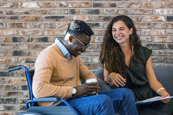 photo of a man in a wheel chair sitting next to a woman on a sofa, both are smiling