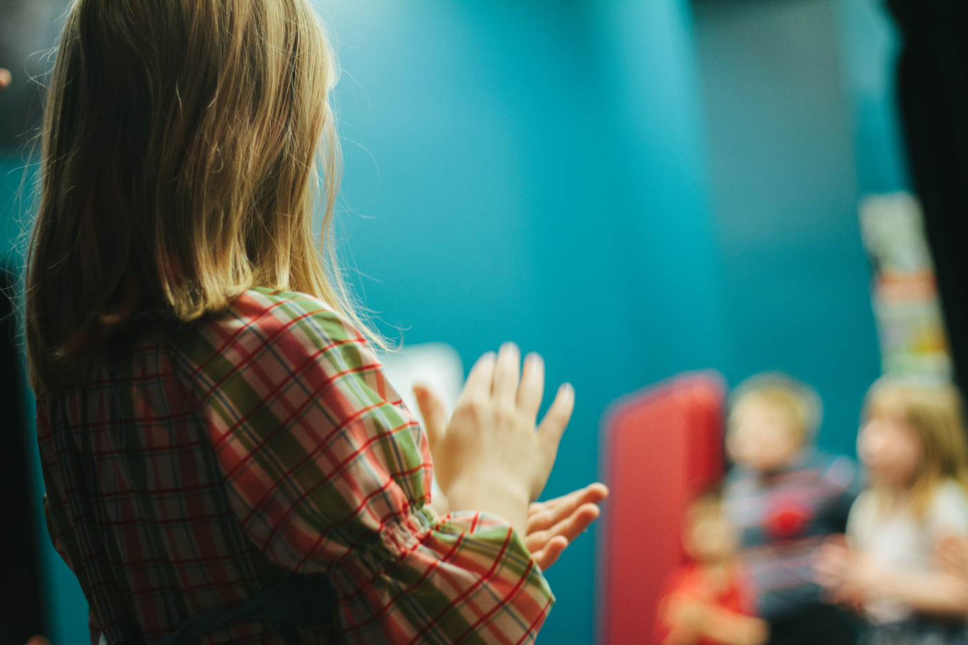 Close up, side view of a woman clapping her hands, with children blurred out in the background