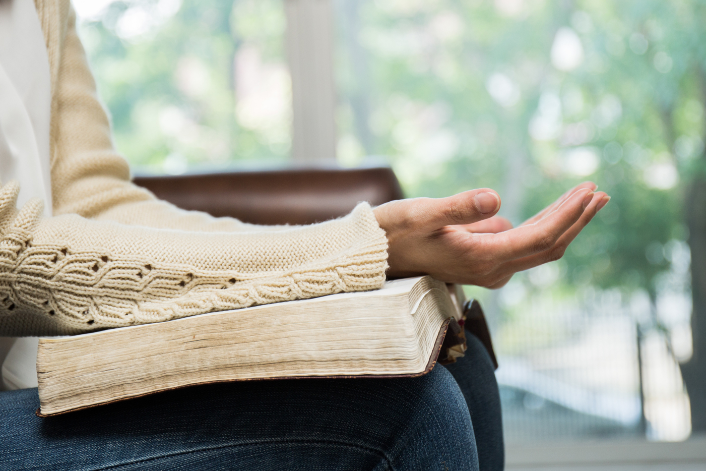 Close up of a woman's legs, with a bible open on her lap, and her arms resting on the bible, palms up as if praying.
