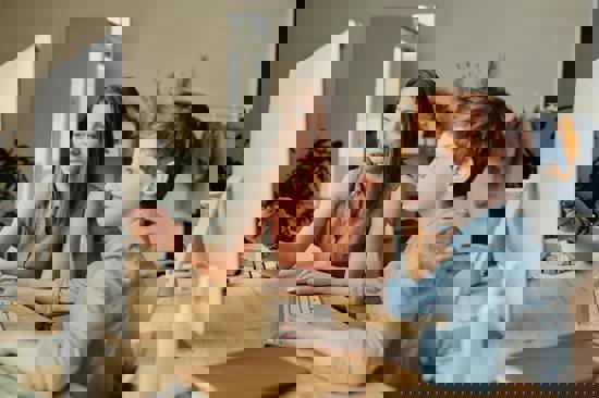 Child using a desktop computer with a women watching